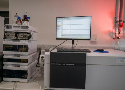 An image of a mass spectrometer, a PC screen displaying graphs and some beakers containing liquid.